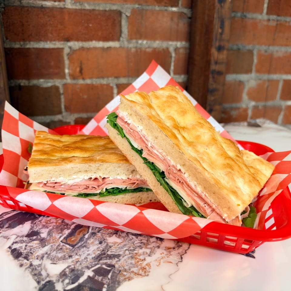 Two toasted ham and cheese sandwiches with lettuce in a red basket lined with checkered paper.