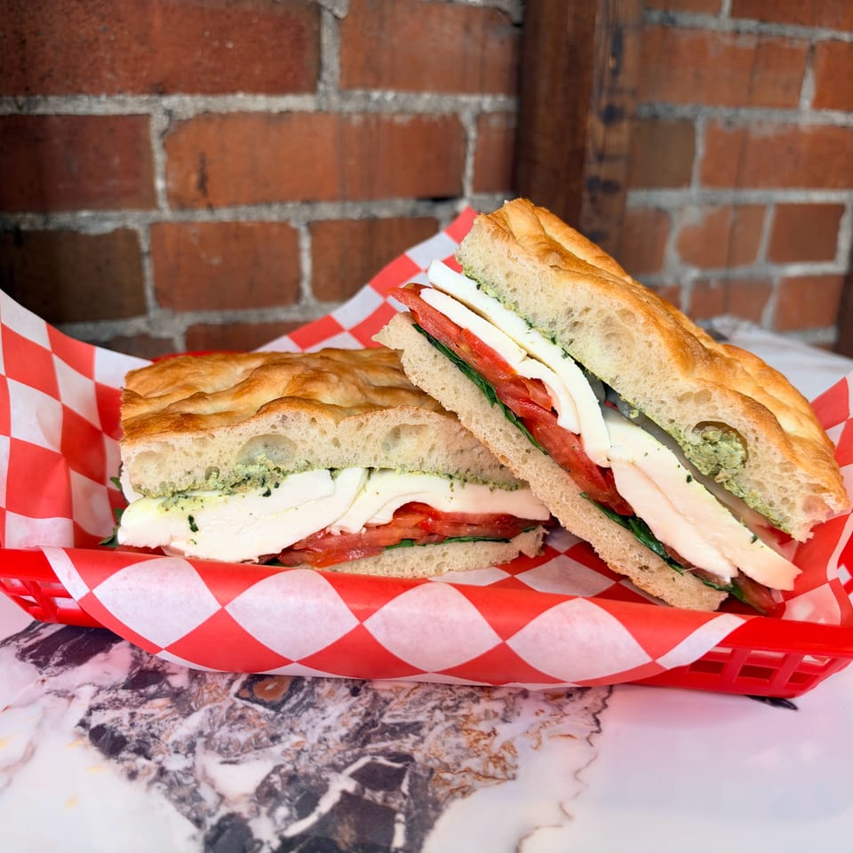Two toasted caprese sandwiches with mozzarella, tomatoes, basil, and pesto served in a red basket lined with checkered paper.
